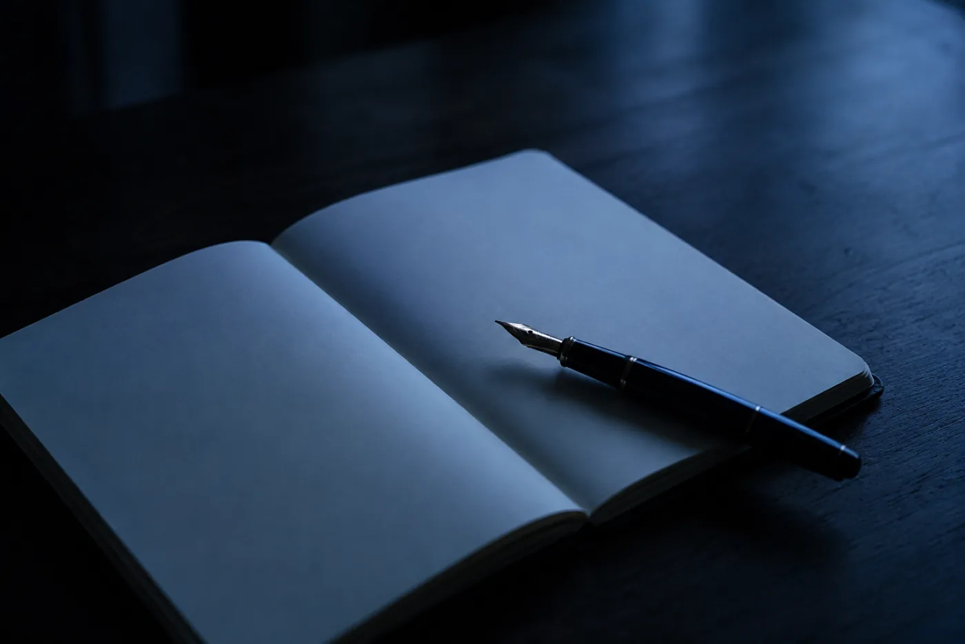 An open notebook with a fountain pen on a dark table at night, the page still blank