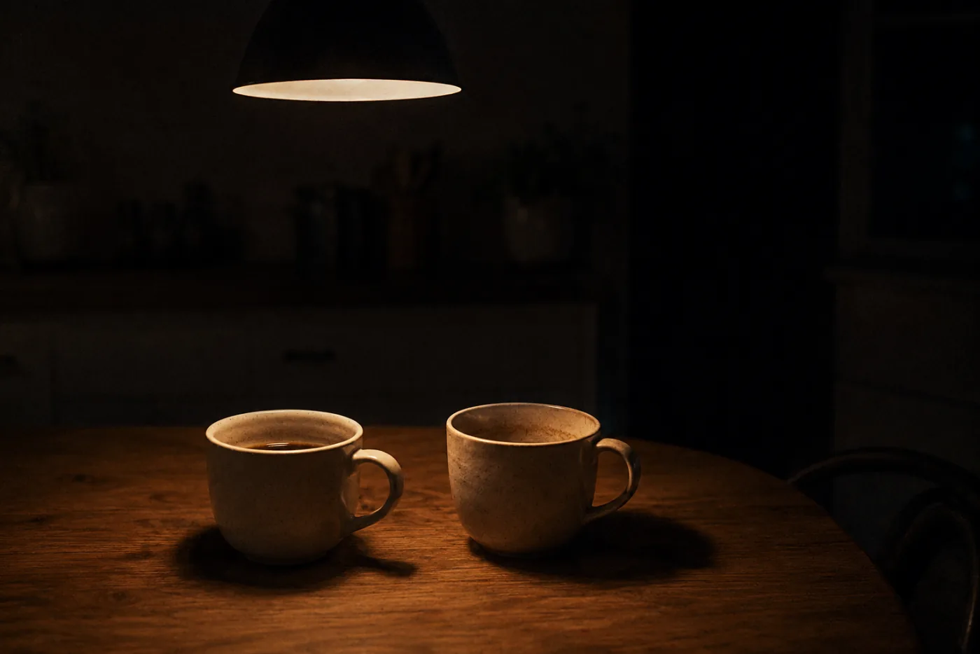 Twee koffiekopjes op een keukentafel onder een lage lamp, laat op de avond